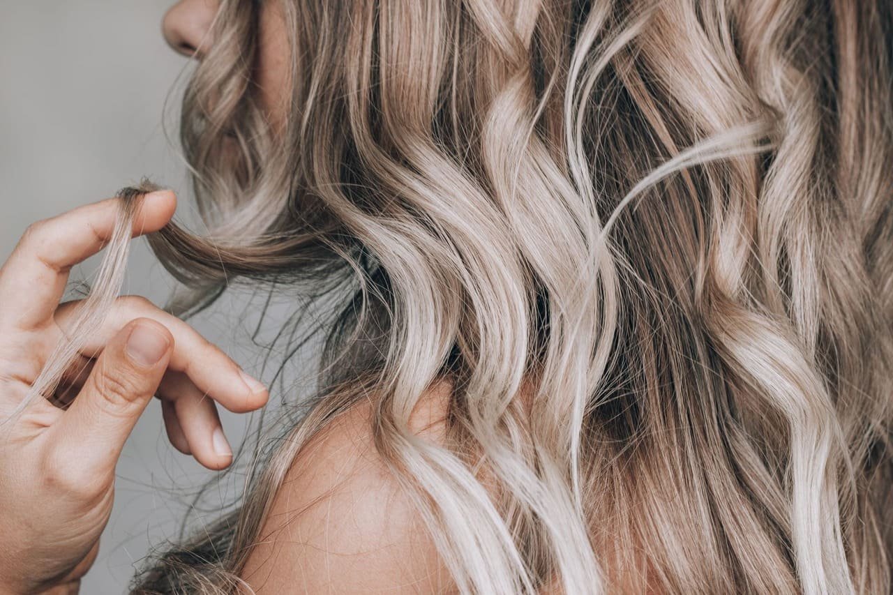 Zbliżenie na kobietę z falowanymi blond włosami, nawijającą na palec kosmyk włosów